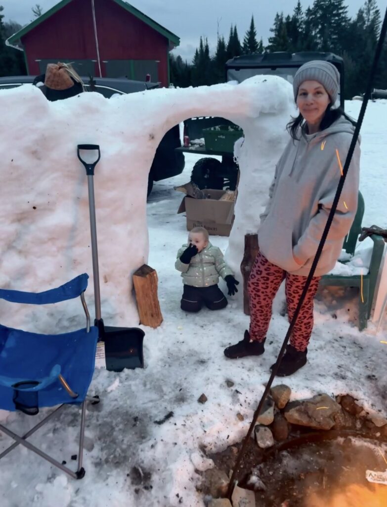 Adult and young child beside a snow igloo near a winter bonfire