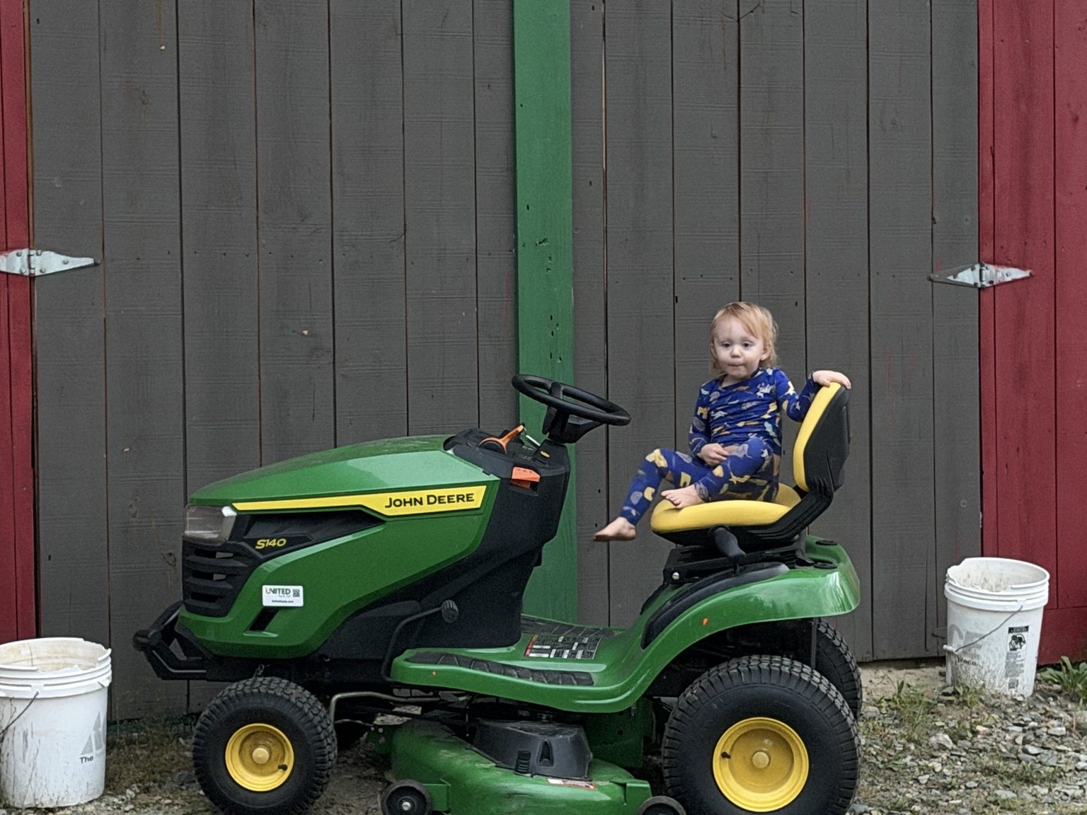 Grandchild sitting on the green John Deere riding mower at the family property