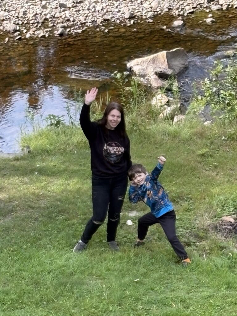 Family members waving beside a small wooded brook